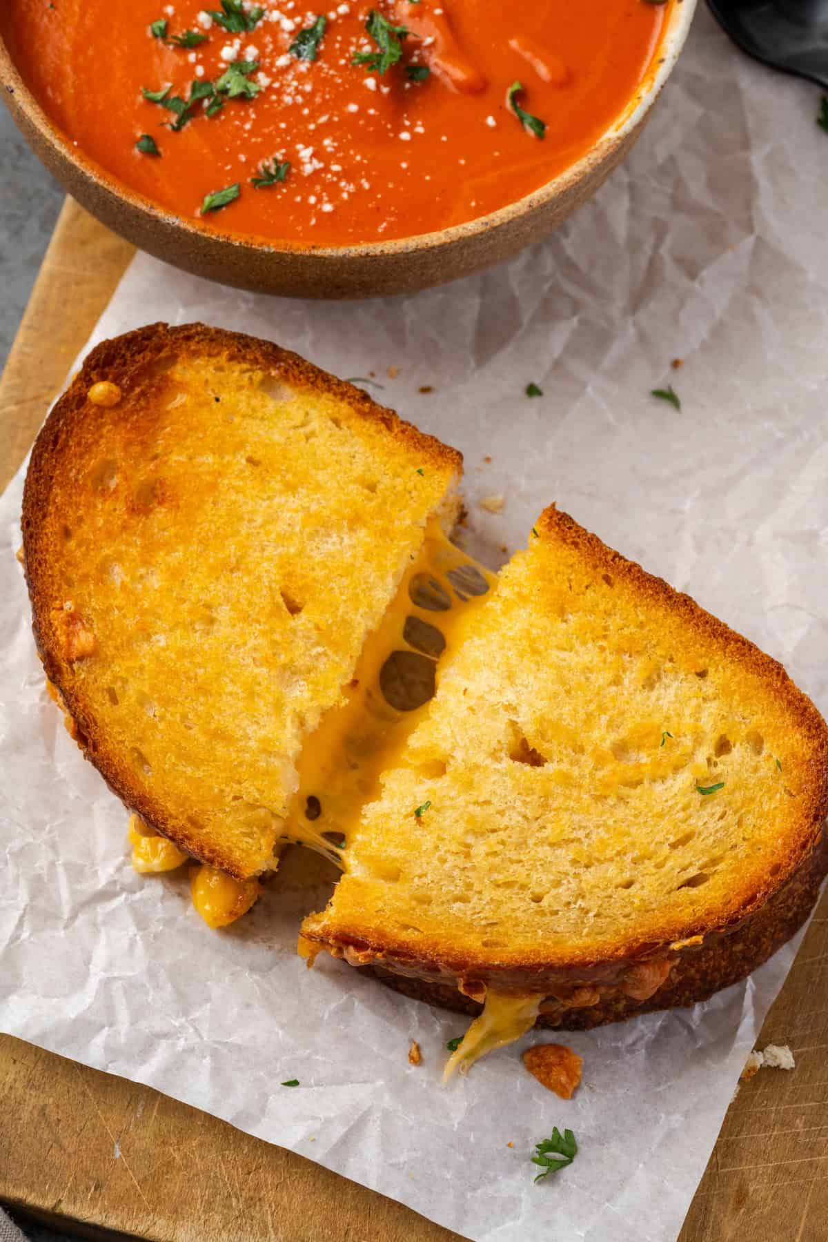 Ce fromage grillé aux frites à air prend des minutes à faire et sort doré à l'extérieur, parfaitement gluant à l'intérieur, avec de grandes cordes de fromage fondant! Gros plan d'un fromage grillé aux frites à air coupé en deux et légèrement séparé pour révéler les cordes de fromage à l'intérieur, à côté d'un bol de soupe aux tomates.