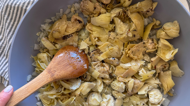 Artichauts et oignons remuant à la main dans la casserole avec cuillère en bois