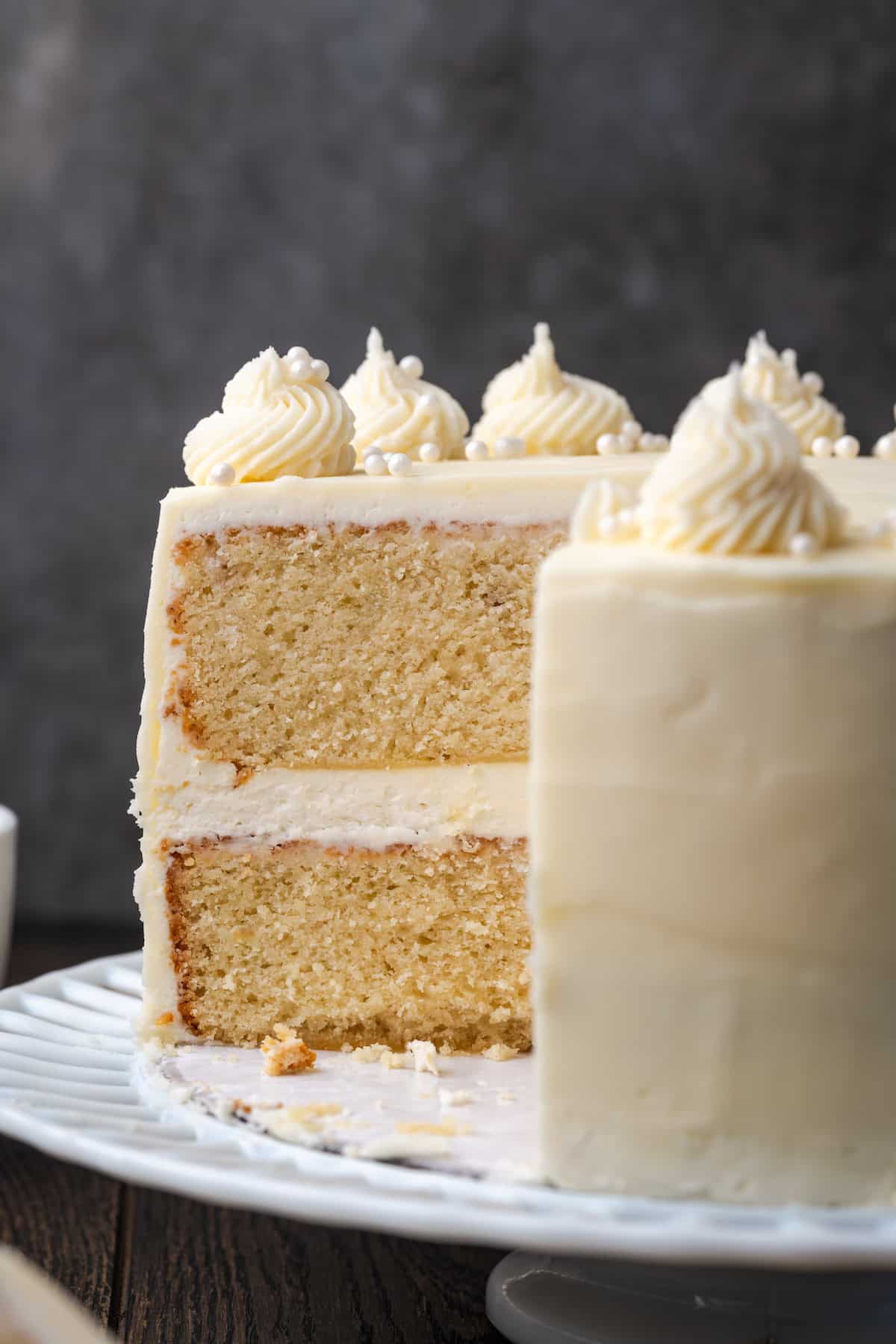 C'est le meilleur gâteau à la vanille à base de zéro! Apprenez à faire deux couches de gâteaux de vanille légères, moelleuses et parfaites givrées de crème au beurre. Vue latérale d'un gâteau à la couche de vanille givrée avec une grande tranche manquante.