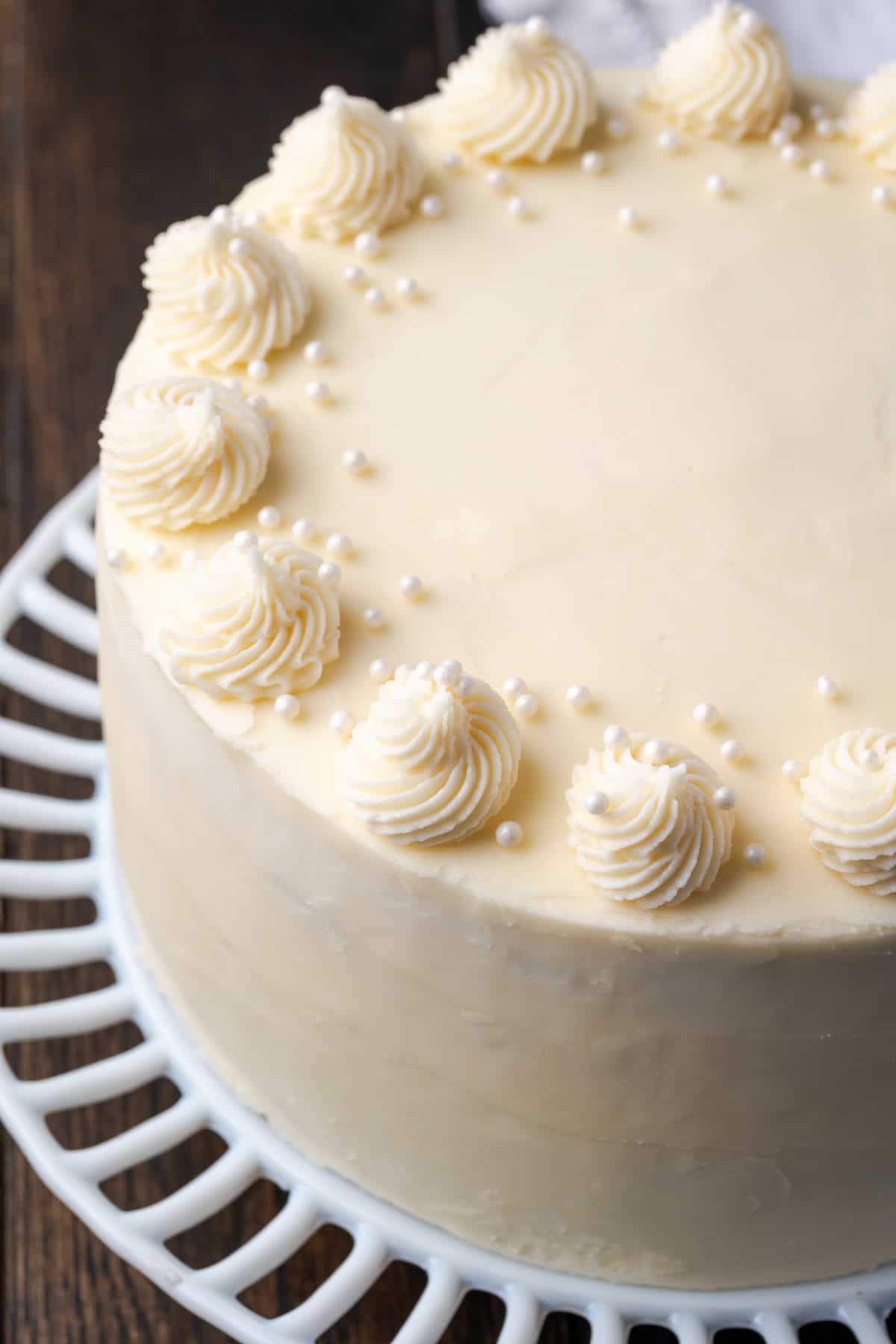 C'est le meilleur gâteau à la vanille à base de zéro! Apprenez à faire deux couches de gâteaux de vanille légères, moelleuses et parfaites givrées de crème au beurre. Vue aérienne d'un gâteau de couche de vanille givrée sur un support à gâteau.