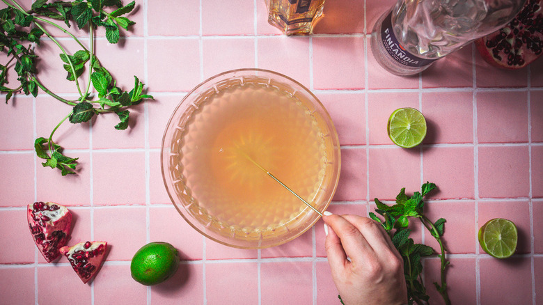 En remuant un grand bol avec du punch rose et garniture tout autour