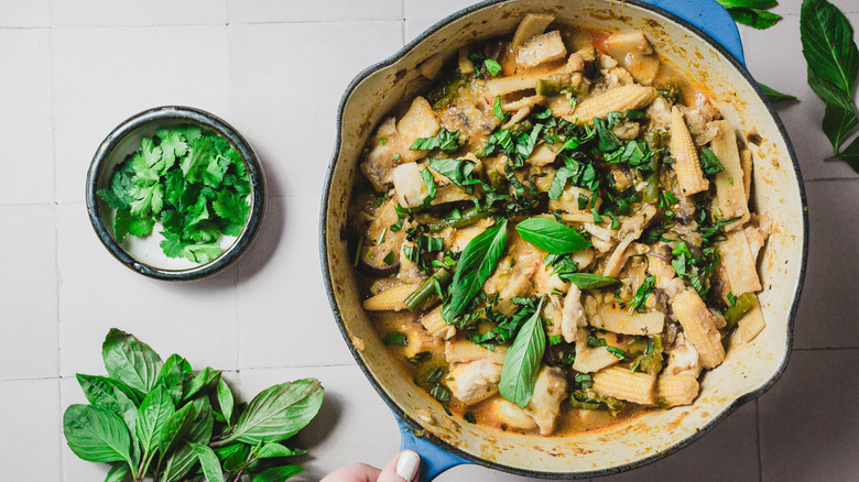 Main tenant une grande poêle avec du curry de poisson avec du basilic thaïlandais