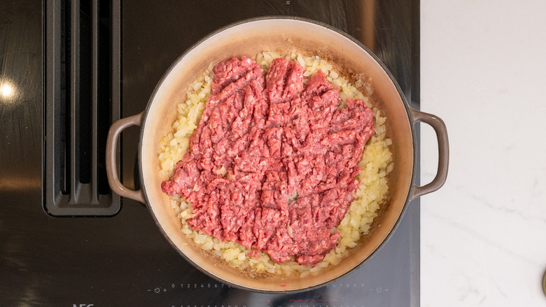 Chuck de bœuf haché cru dans la poêle sur les oignons en dés