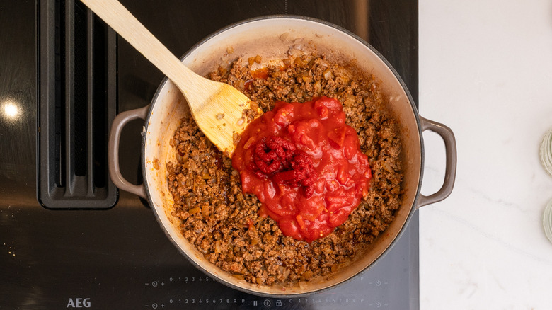 Les tomates en conserve, la pâte de tomate et la bière ambre ajoutée à une poêle avec du bœuf cuit et des oignons