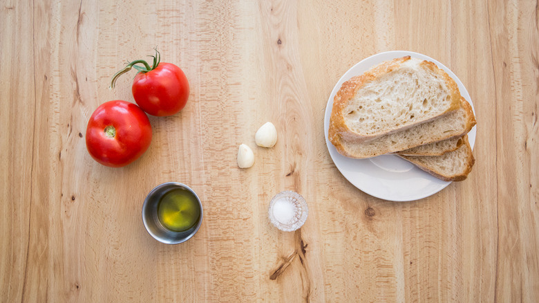 Tomates, gousses d'ail, bol de sel, bol d'huile d'olive et tranches de pain dans l'assiette disposée