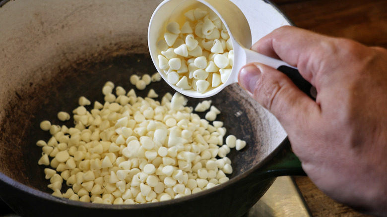 pépites de chocolat blanc versant de la tasse à mesurer dans un pot sur le poêle