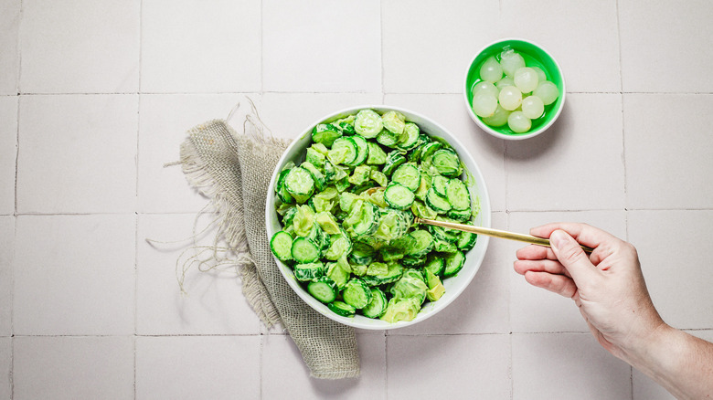 Main soulevant une fourchette de salade de concombre avocat du bol
