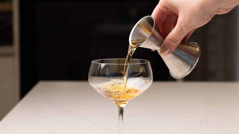 Main à l'aide d'un jigger pour verser du liquide dans un verre à cocktail