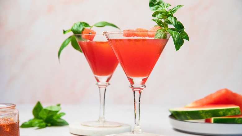 Deux verres à martini pastèque avec de l'huile et des tranches en arrière-plan.