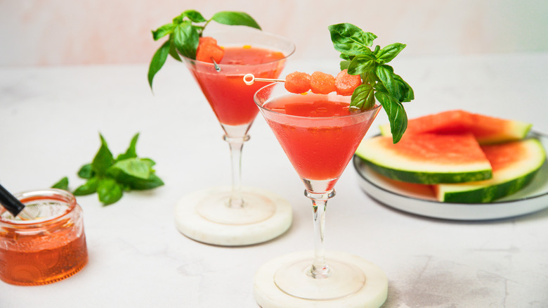 Deux verres à martini pastèque avec de l'huile et des tranches en arrière-plan.